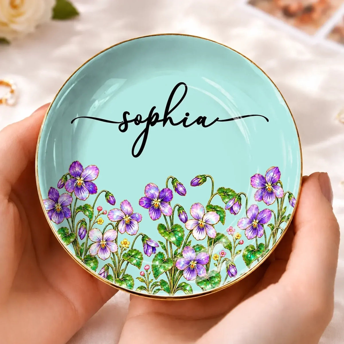 Round turquoise jewelry dish with purple flowers and the name Sophia, held in two hands
