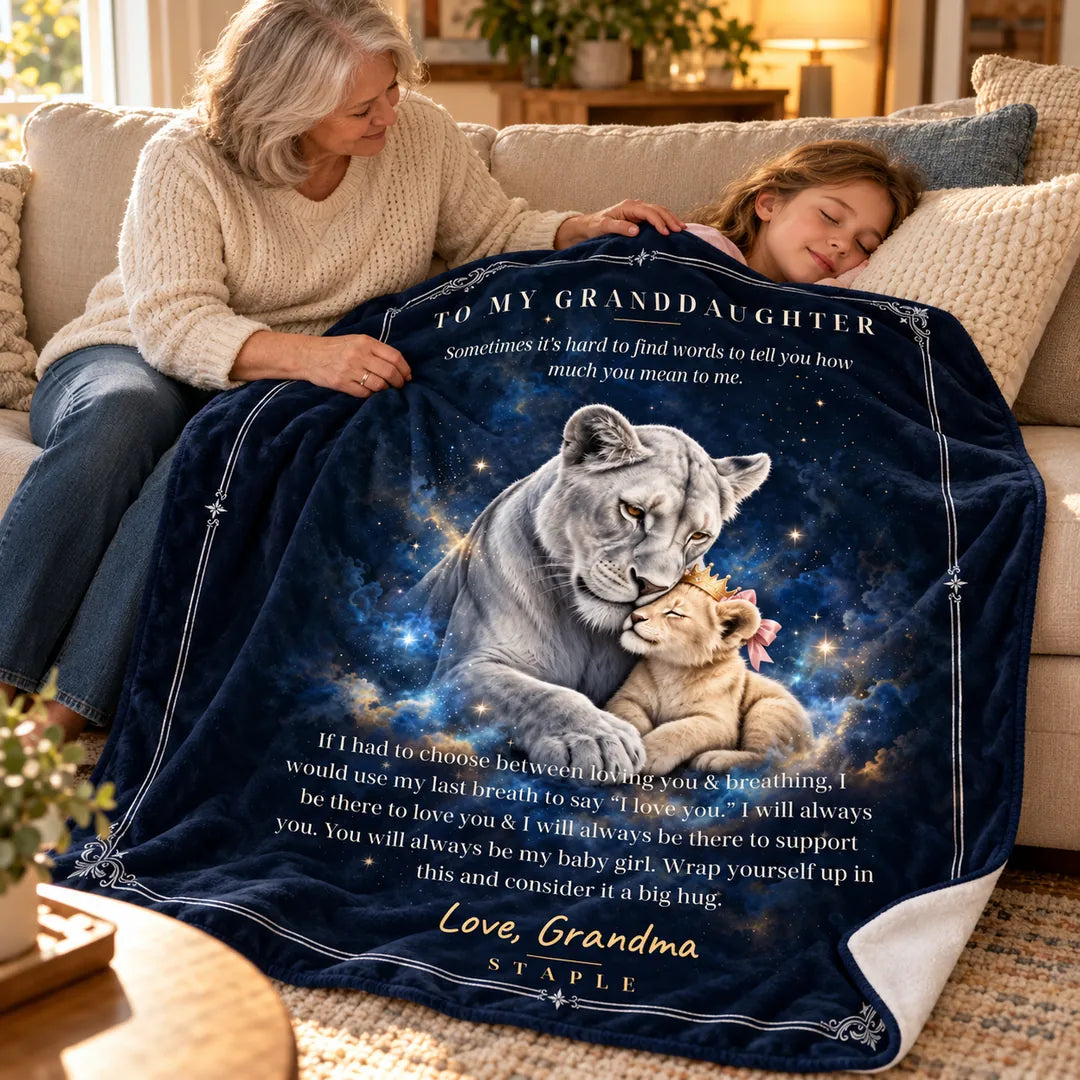 Grandmother gently tucking the navy lion blanket around her sleeping granddaughter on a sofa, with Love, Grandma message.