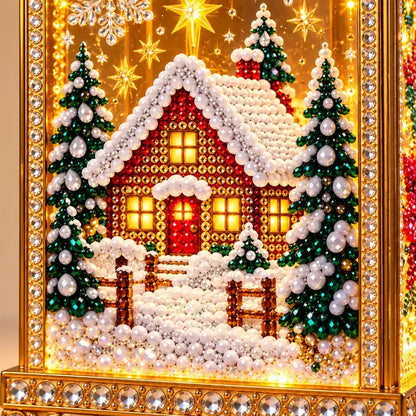 Illustrative product view: Close-up of the completed lantern's snowy cottage artwork, showing faceted gems, evergreen trees and gold-and-crystal trim.