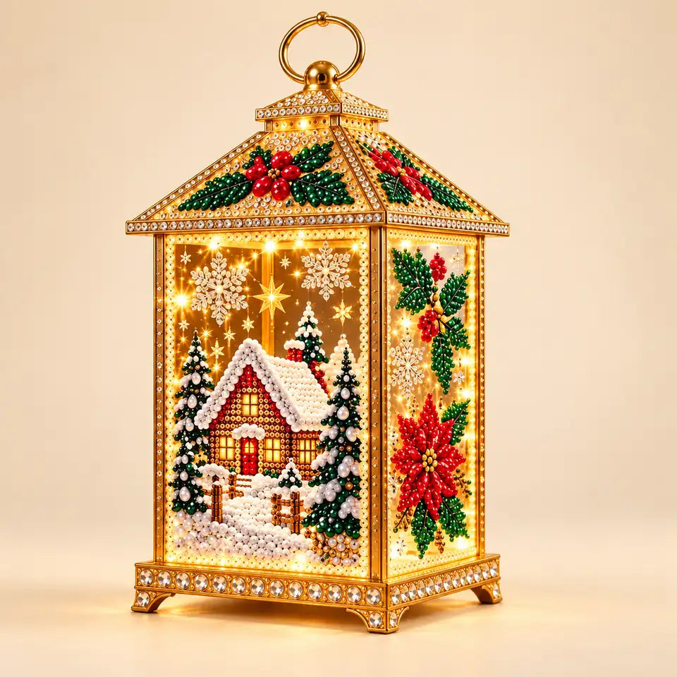 Illustrative studio view: Completed diamond-art lantern on an ivory background, showing the snowy cottage front, holly and poinsettia side, gold frame and ring handle.