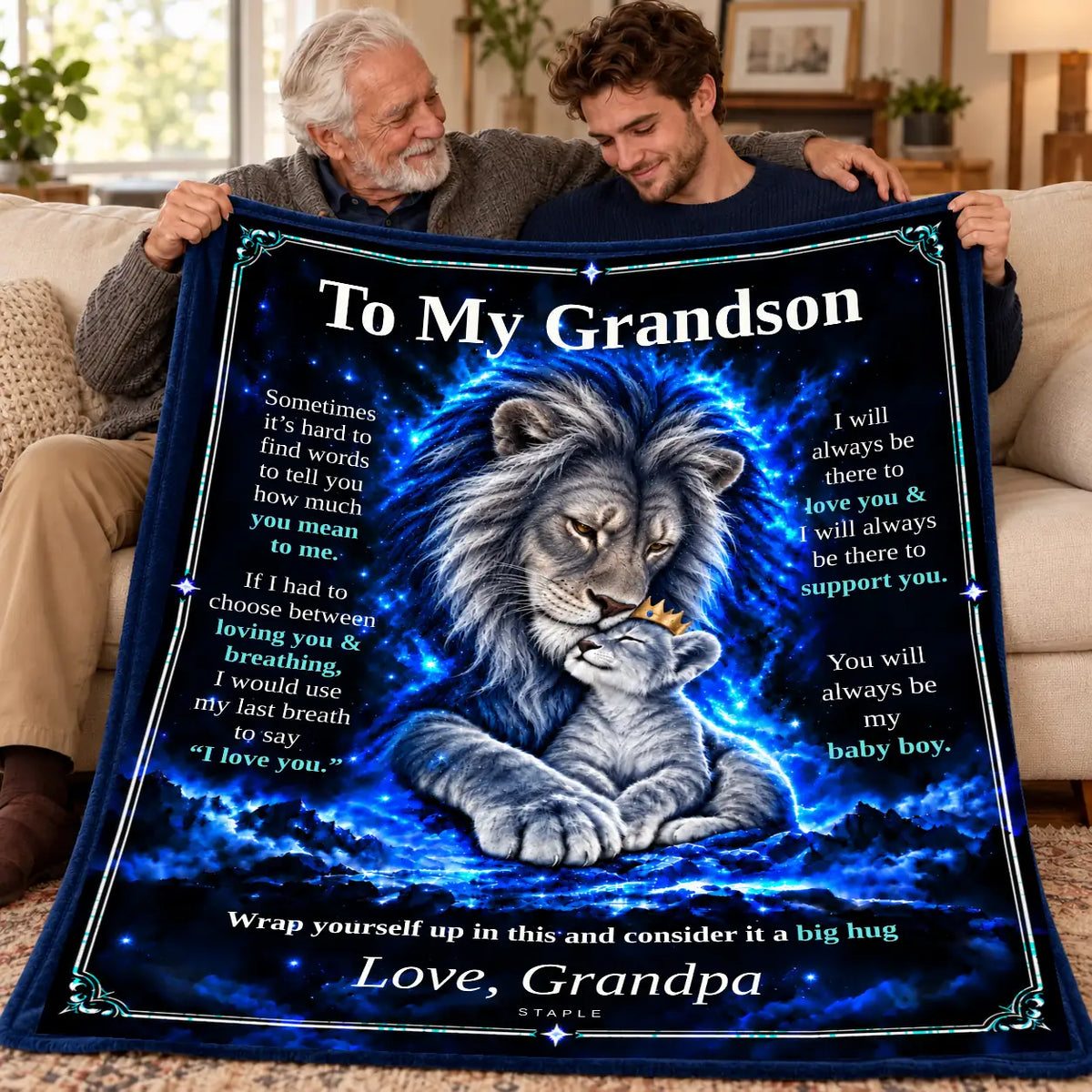 Illustrative lifestyle mockup: To My Grandson lion blanket held by a grandfather and adult grandson on a sofa, showing the Original Blue artwork and Love, Grandpa signature.