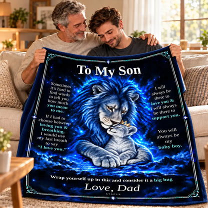 Illustrative lifestyle mockup: To My Son lion blanket held by a father and adult son on a sofa, showing the Original Blue artwork and Love, Dad signature.